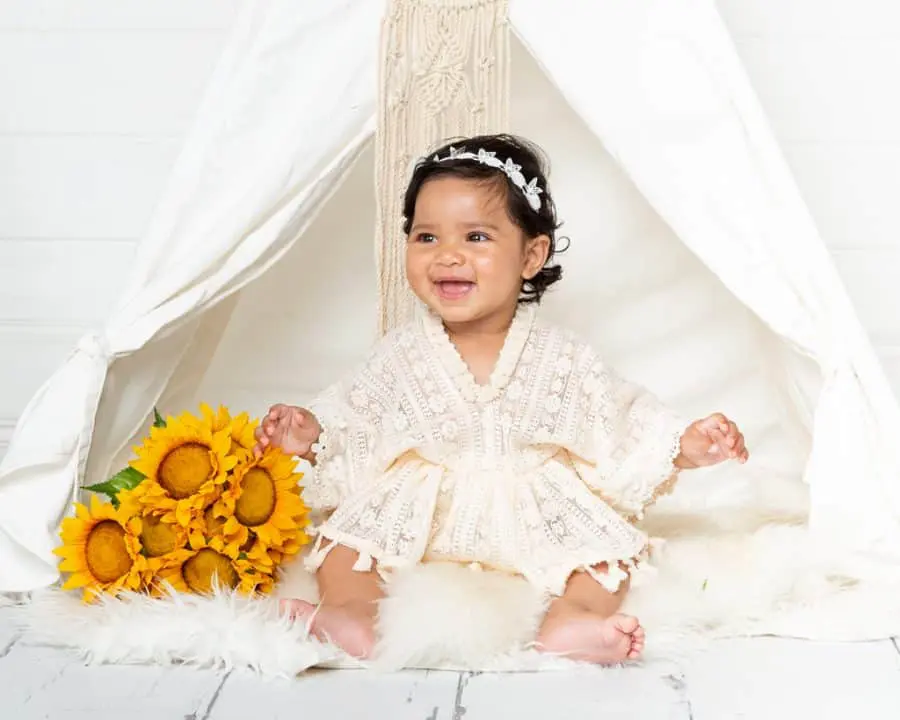 a little girl is laughing while wearing a lace outfit and sitting with some sunflowers
