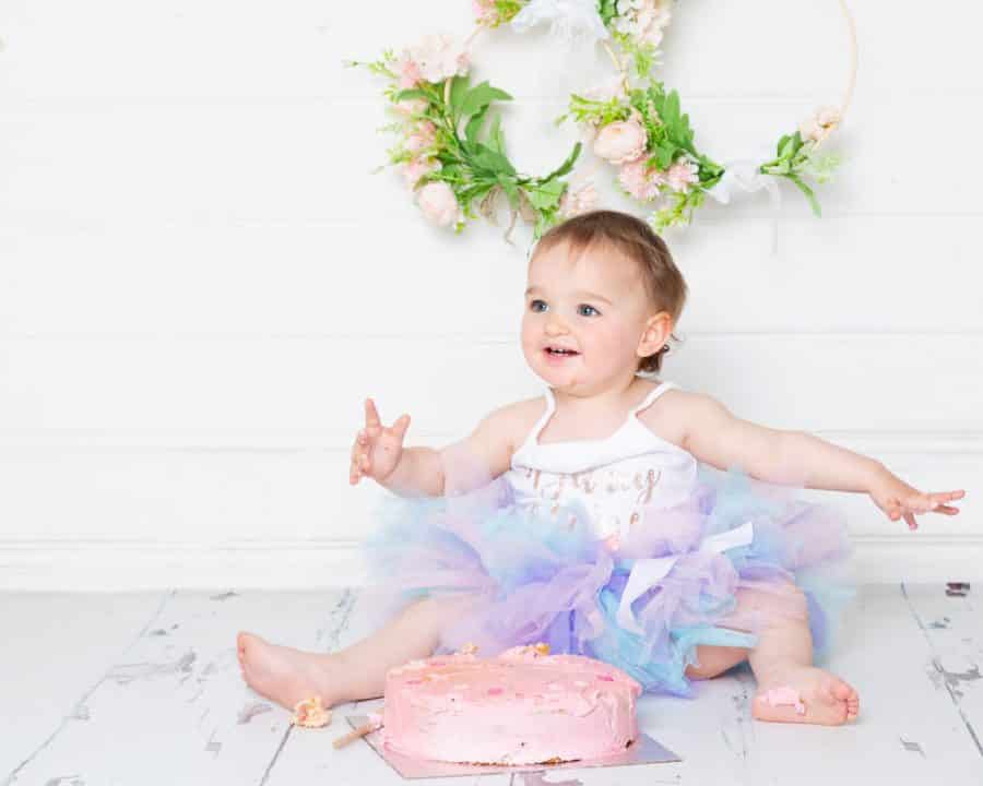 A little girl in a pastel tutu is enjoying herself as she gets into her cake smash photo shoot