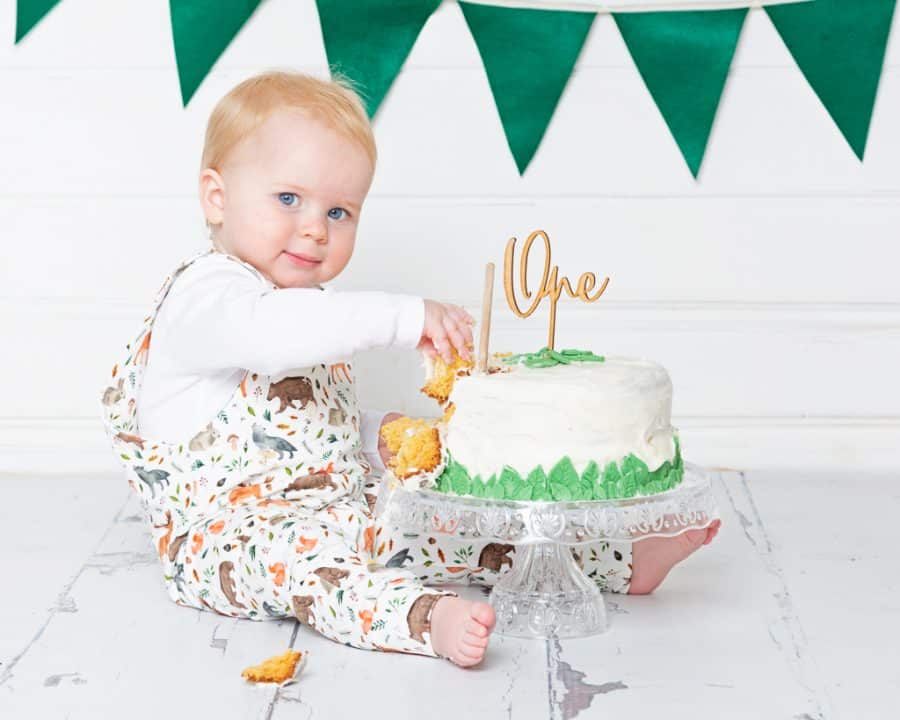 a little boy sits with his cake on a stand at his first birthday shoot