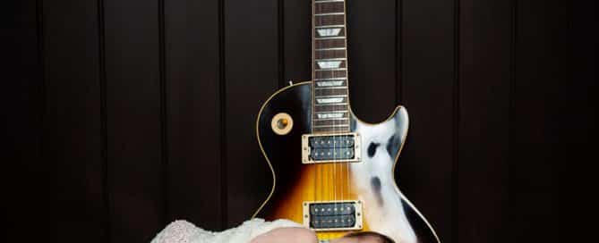 a newborn is partially swaddled and lying on a guitar case with a guitar behind him. He is smiling