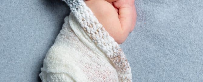 a sleeping newborn in a cream long tail hat