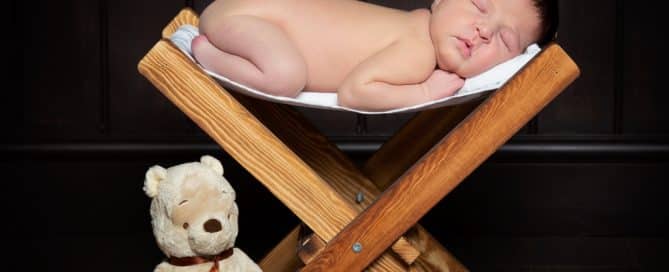 a baby sleeping on a small wooden hammock with a teddy bear