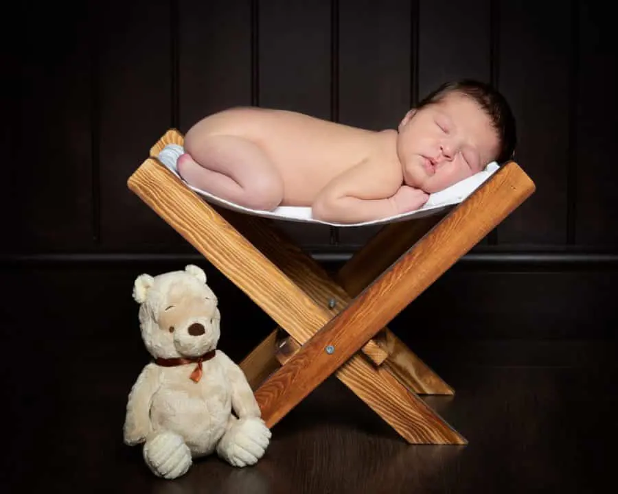 a baby sleeping on a small wooden hammock with a teddy bear