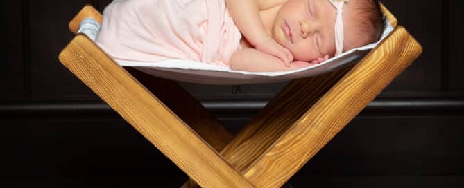 a little girl sleeps on a wooden hammock with peach flowers