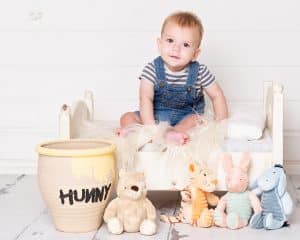 Baby Photography East Grinstead West Sussex a baby poses on a white bed with a Hunny pot and Winnie the Pooh themed stuffed toys