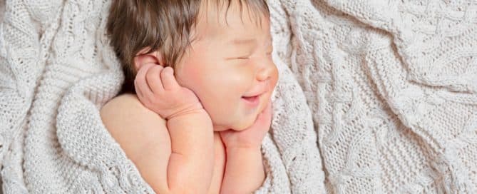 a sleeping newborn smiles wrapped in a cream blanket