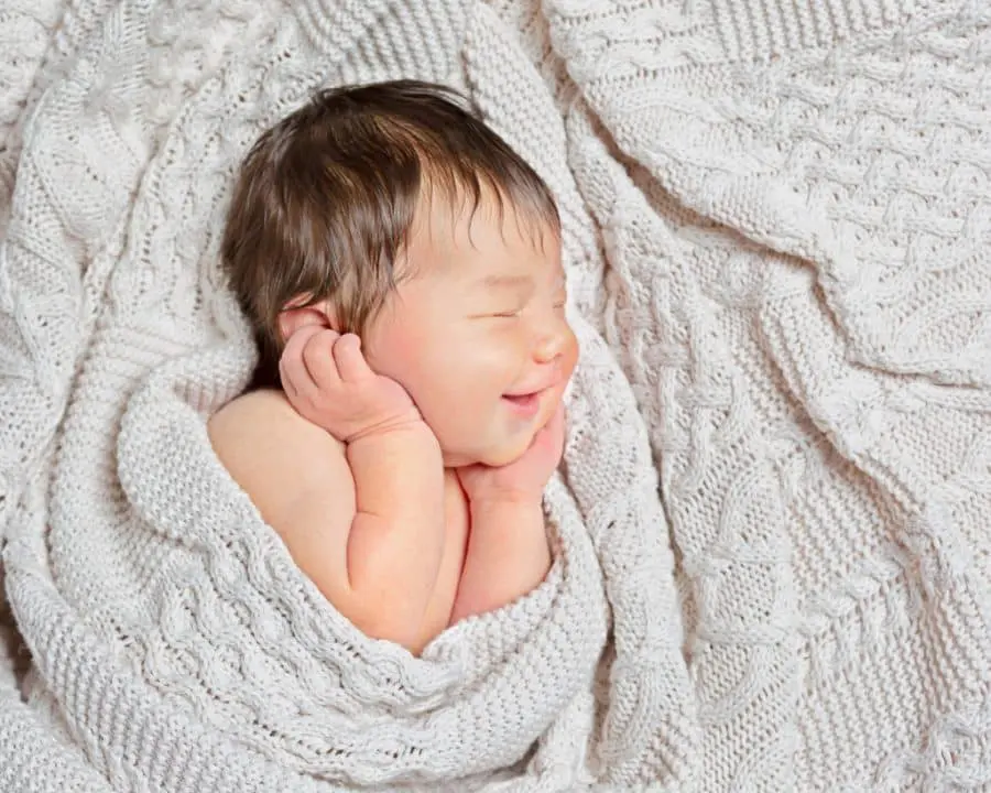 a sleeping newborn smiles wrapped in a cream blanket