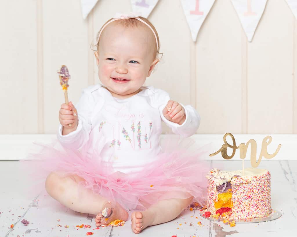 a little girl in a pink tutu sits by her cake at her first birthday photo shoot