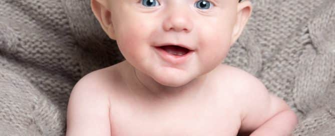 a little boy in a flat cap laughs at the camera against a grey blanket