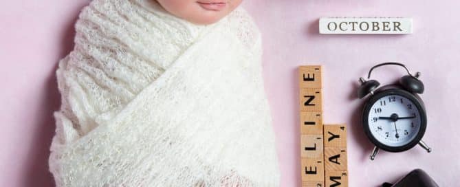 a smiling newborn asleep wrapped in white on a pink background with birth announcement details