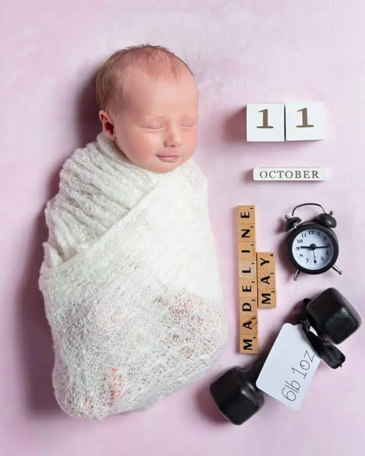 a smiling newborn asleep wrapped in white on a pink background with birth announcement details