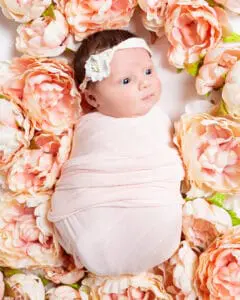 Newborn Photography East Grinstead West Sussex a newborn swaddled in peach sleeping in peony flowers
