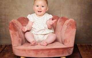 a baby sits in a pink chair against a fine art brown canvas backdrop