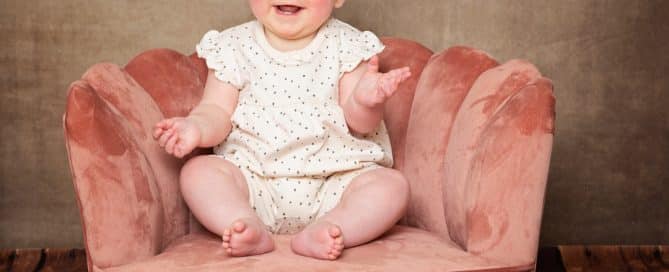 a baby sits in a pink chair against a fine art brown canvas backdrop