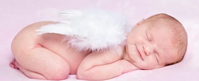 a newborn wearing feather angel wings on a pink blanket