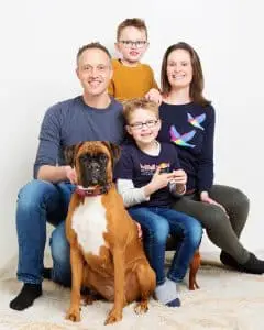 a family poses with two boys and a boxer dog