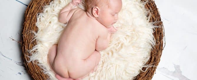 a newborn sleeping in a nest prop with a fluffy white blanket