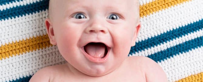 a very happy baby boy on a green and yellow striped blanket