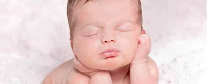 a newborn sleeps with their head propped up on their hands