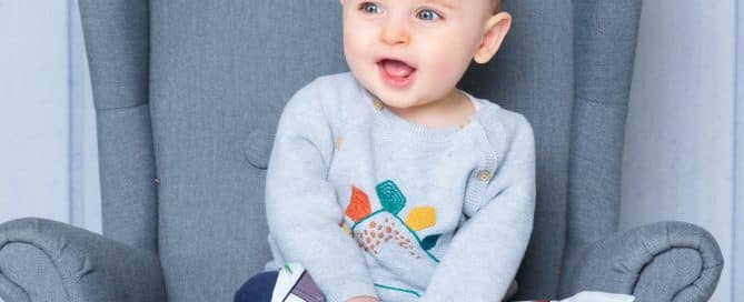 a baby sits in a chair reading a pretend newspaper