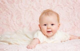 a little girl in a christening dress against a pink blanket backdrop