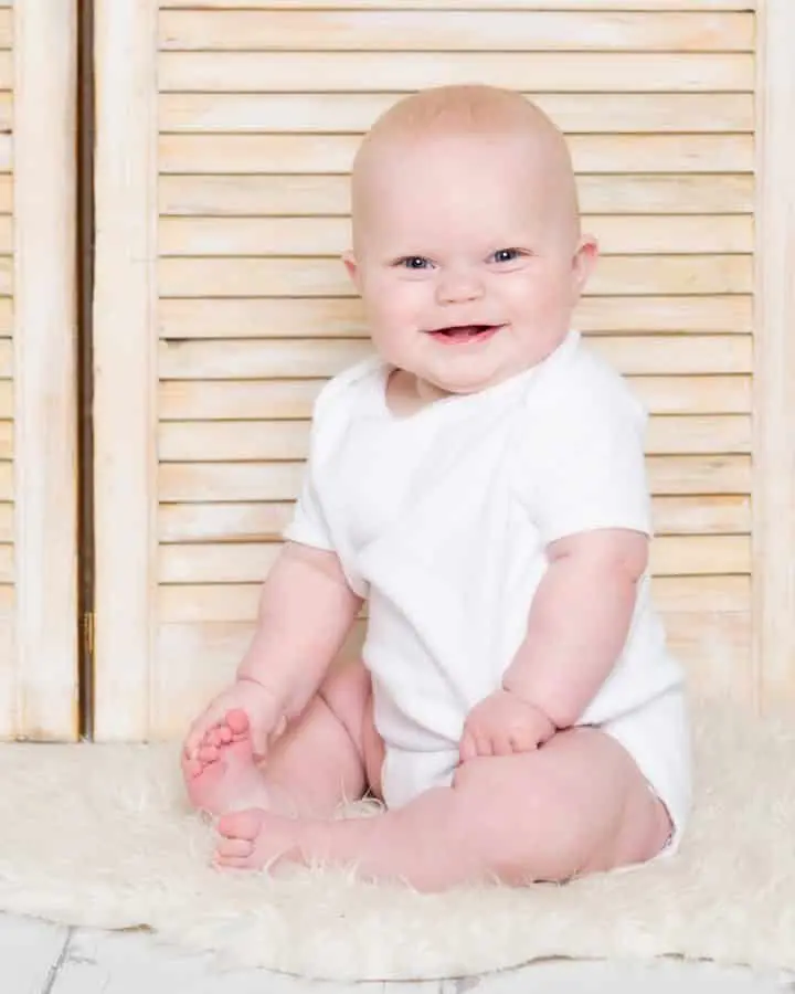 a baby in a classic white vest against some light wood shutters