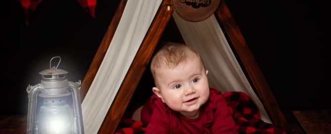 a baby in a miniature camping tent prop set against a black background