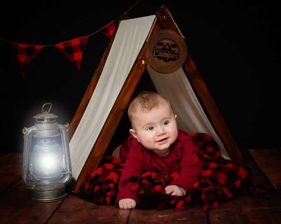a baby in a miniature camping tent prop set against a black background