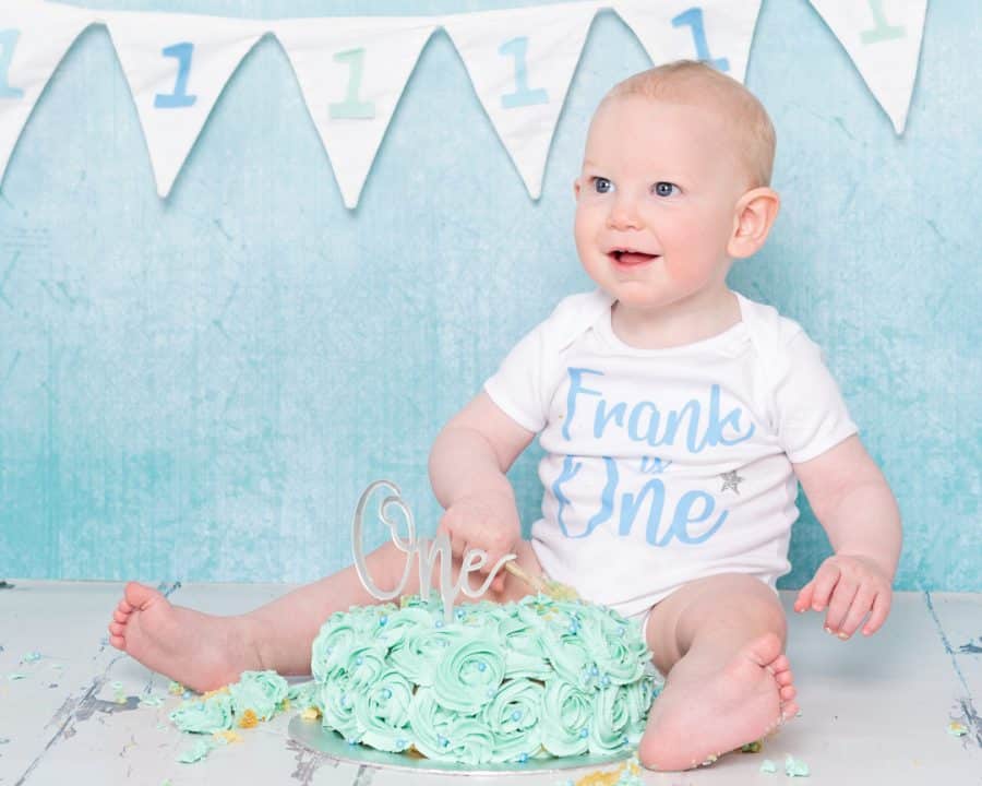 A boy sits in front of a light blue background with his birthday cake