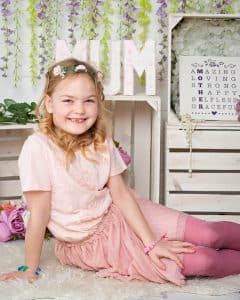 a little girl sits and smiles at the camera at a mother's day photo shoot event 