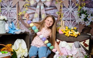 a little girl posted with a happy easter sign at a bunny themed easter photo shoot set