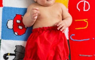 a little boy in red shorts lies on a personalised handknitted blanket