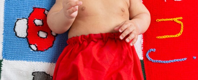 a little boy in red shorts lies on a personalised handknitted blanket