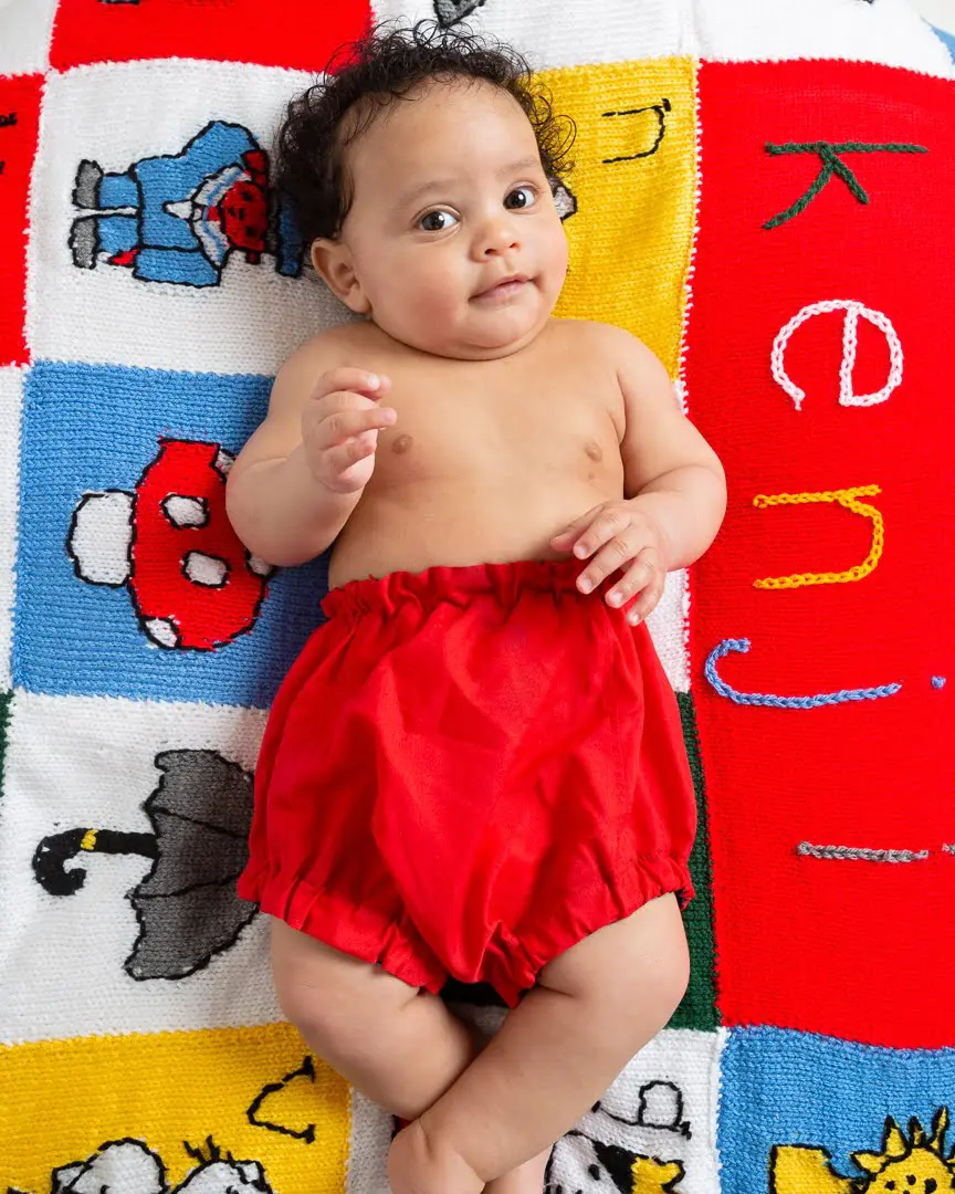 a little boy in red shorts lies on a personalised handknitted blanket