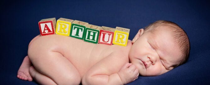 a newborn named arthur with letter blocks on their back against a blue background