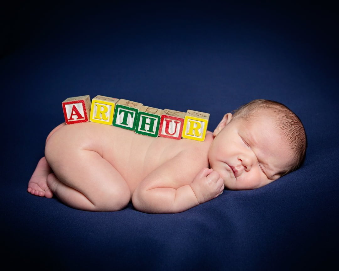 a newborn named arthur with letter blocks on their back against a blue background