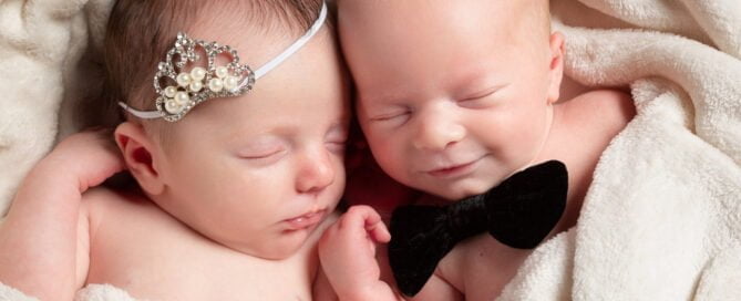 newborn twins sleep together, the girl wearing a tiny tiara and the boy with a tiny bow tie