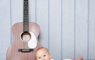 a baby in a vest lying next to a brown guitar