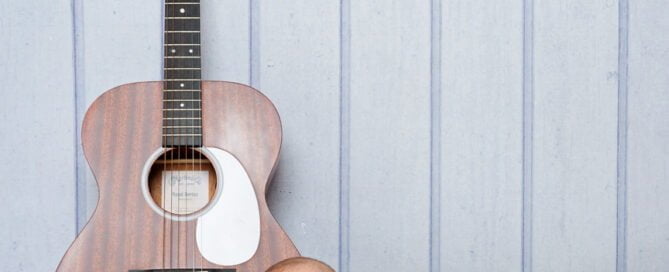a baby in a vest lying next to a brown guitar