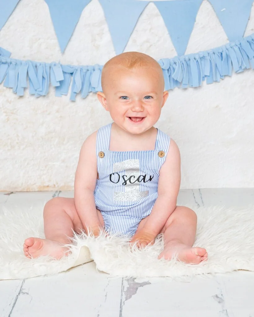 a happy little boy in a blue and white striped romper at his first birthday photo shoot