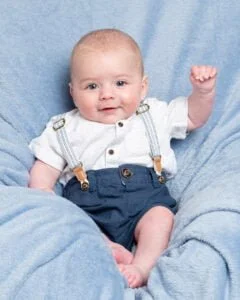 a little boy waves at the camera on blue blanket