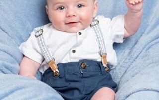 a little boy waves at the camera on blue blanket