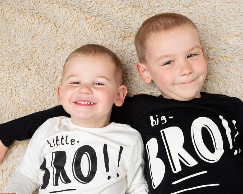 Two brothers lie on the ground looking up at the camera with cheeky grins