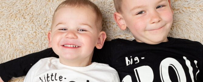 Two brothers lie on the ground looking up at the camera with cheeky grins
