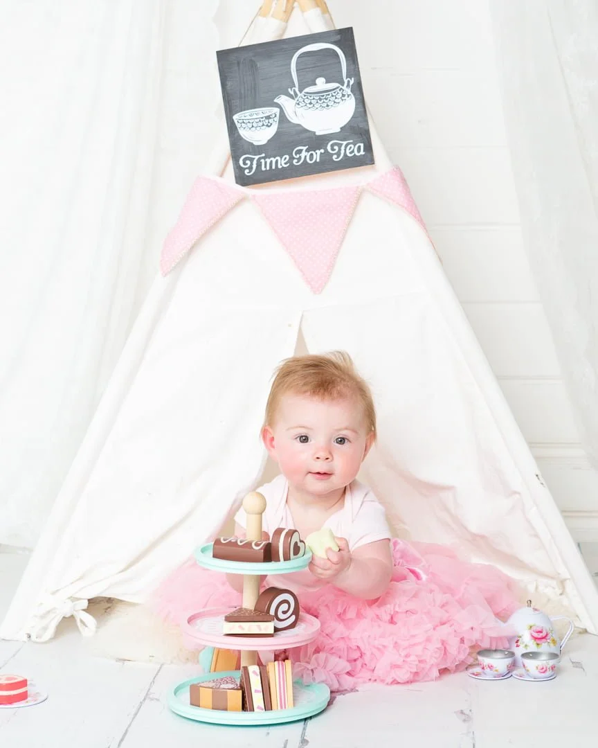 a little girl in a tutu poses with tea props in a teepee