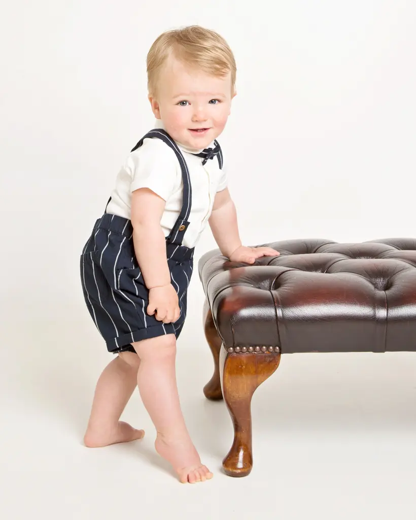 a little boy poses next to a footstool in a pinstripe outfit
