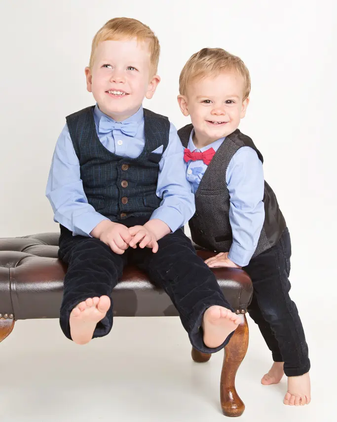 two brothers pose for a photo - one sitting on a footstool and one standing beside it