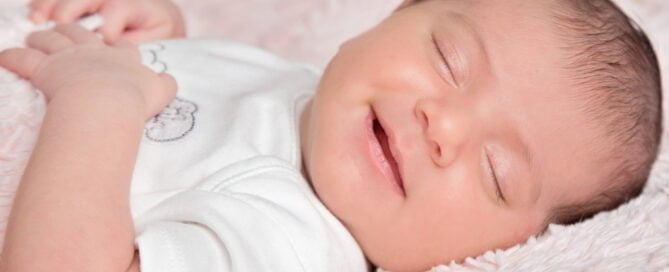 a newborn girl sleeps on a pink blanket and smiles gently