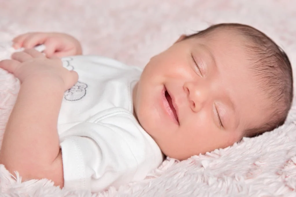 Newborn Photography East Grinstead West Sussex a newborn girl sleeps on a pink blanket and smiles gently