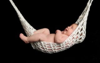 a newborn sleeping in a string hammock against a black background